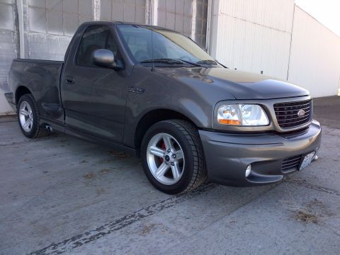 2003 Ford F-150 - A dark gray Ford F-150 Lightning pickup truck is parked on a concrete surface in front of a building.