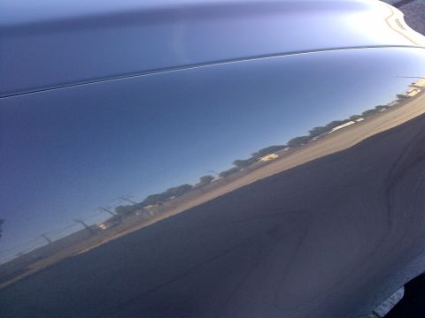 2003 Ford F-150 - Reflections on a dark blue car hood show a road lined with trees and utility poles.