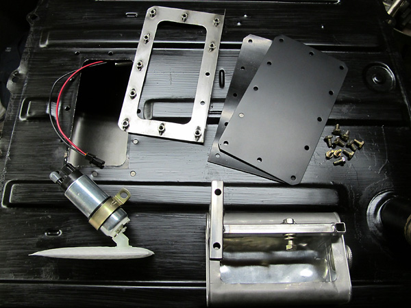 Fuel pump with filter, metal mounting bracket, two black plates, and screws on a black textured surface