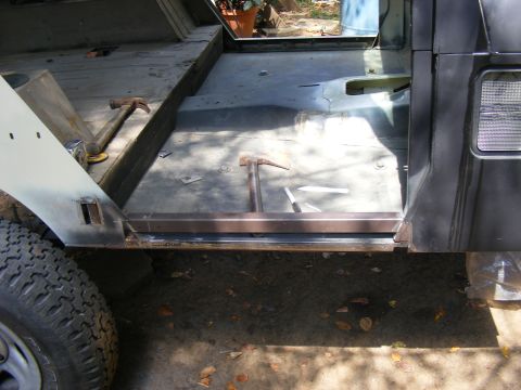 Interior of a vehicle undergoing repair, showing floor pan and door frame. Hammers are on the floor