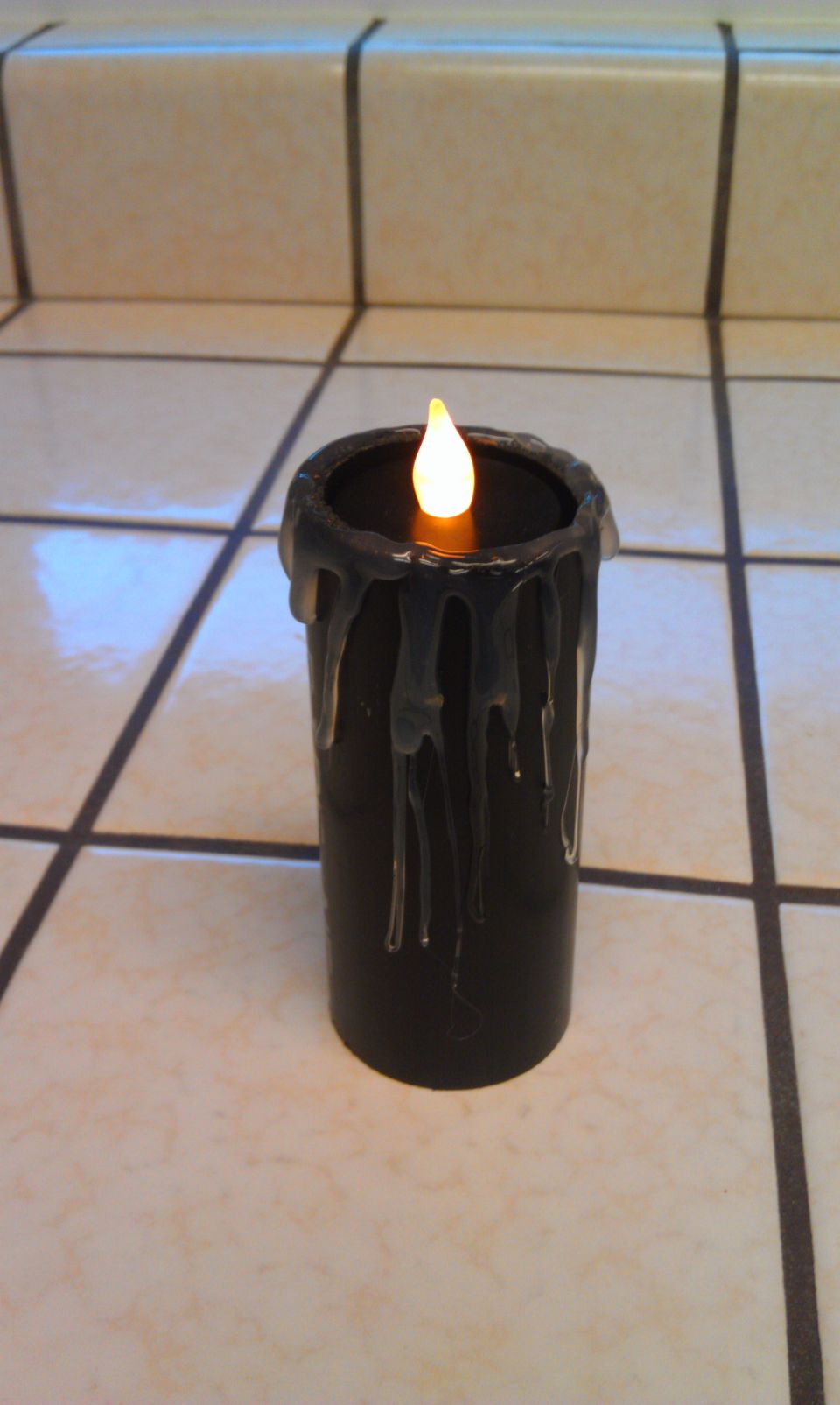 Black candle with dripping wax effect and an artificial flame sits on a tiled surface