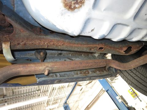 1991 Ford LTD Crown Victoria - The undercarriage of a vehicle, with significant rust on the frame and exhaust system, is shown from a low angle.