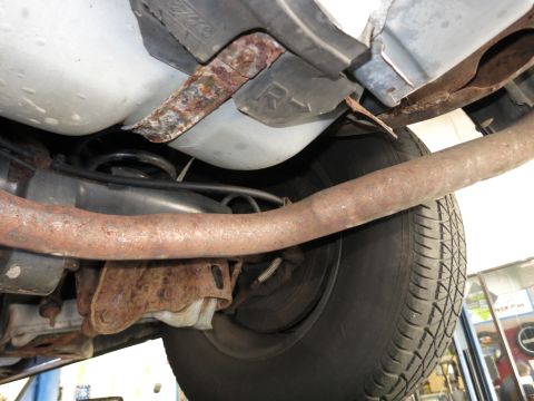 1991 Ford LTD Crown Victoria - Close-up of rusty exhaust and suspension parts underneath a vehicle, with a tire visible.