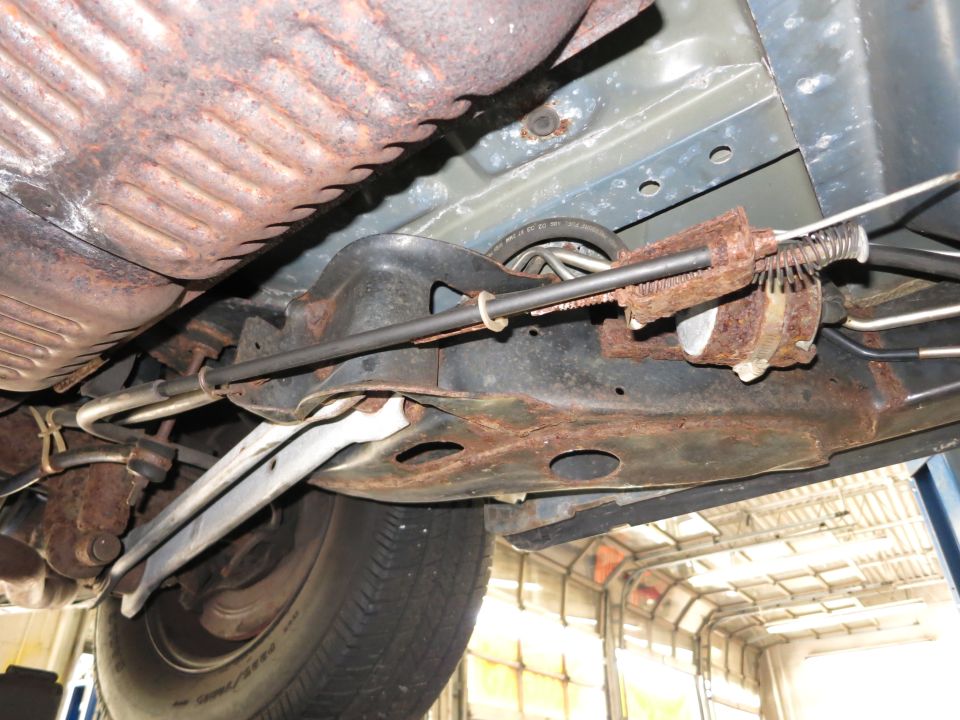 Underside of a vehicle showing rusty suspension components and exhaust system