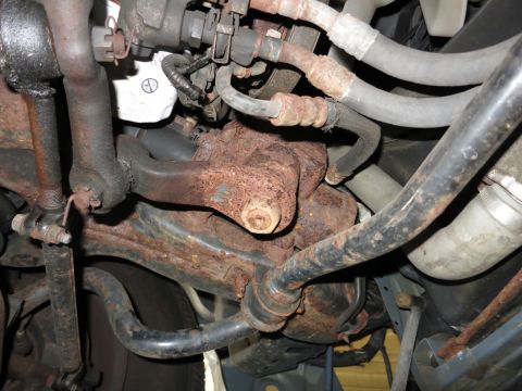 1991 Ford LTD Crown Victoria - Close-up view of heavily rusted engine and suspension parts under a vehicle.