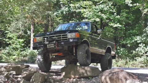 1987 Ford Bronco - A black 1987 Ford Bronco navigates a rocky trail with its suspension lifted high.