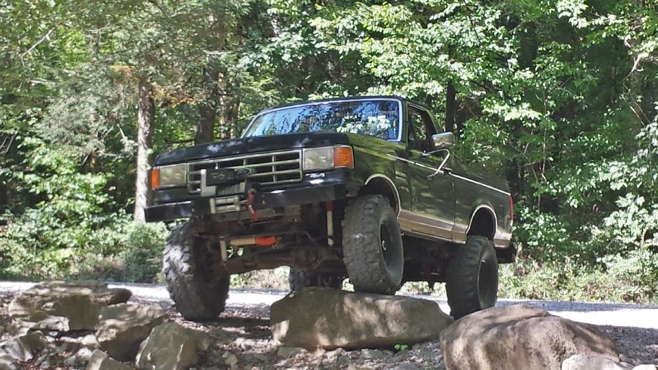Black 1987 Ford Bronco with lifted suspension and large tires driving over rocks