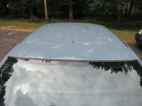 1991 Ford LTD Crown Victoria - The car roof has three studs, and the rear window reflects trees and clouds.
