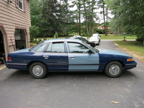 1991 Ford LTD Crown Victoria - A sedan with a mismatched paint job is parked in front of a garage, with other vehicles in the background.