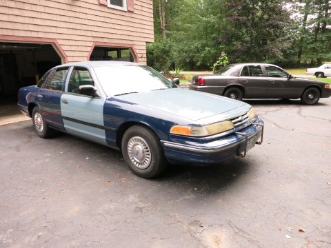 1991 Ford LTD Crown Victoria - A two-tone blue sedan is parked in front of a garage, with another sedan visible in the background.