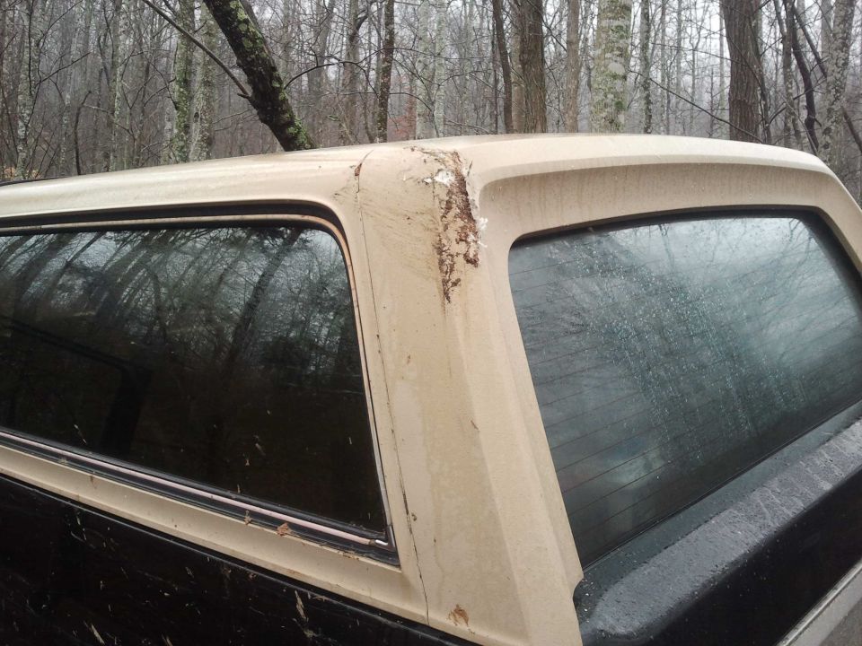 Tan truck cap with peeling paint and rust on a dark vehicle, seen from the side