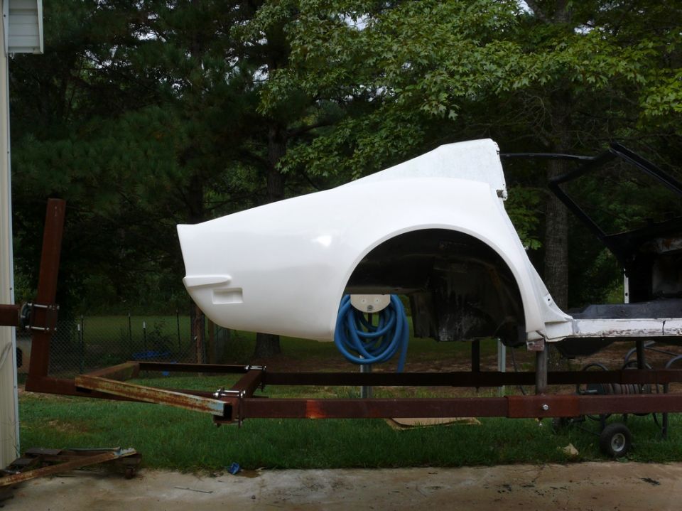 White car body panel, likely a fender, mounted on a trailer outdoors