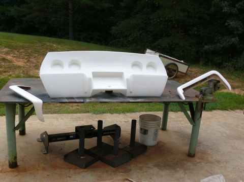 1976 Chevrolet Corvette - A white fiberglass rear bumper, likely for a C3 Corvette, is displayed on a workbench with various tools and parts nearby.