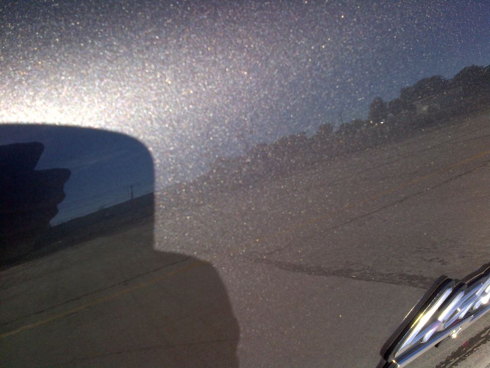 Close-up of dark metallic paint with visible flake. Reflection of a person and a pole in the curved surface