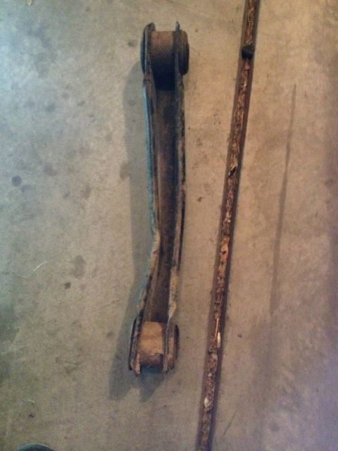 2005 Jeep Wrangler - A single control arm and a long, rusty metal strip lie on a concrete surface. The part appears to be automotive.