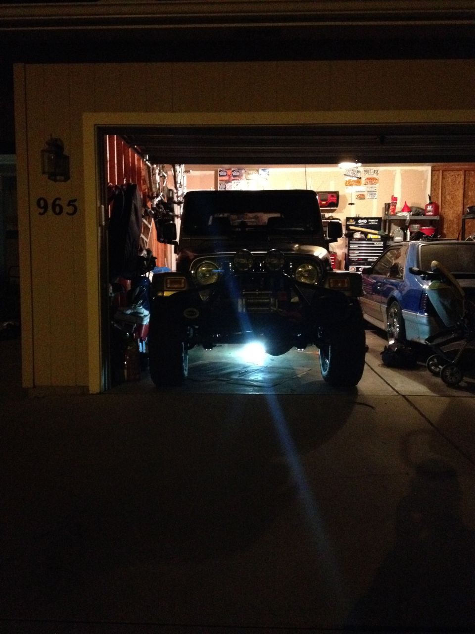 Front view of a dark Jeep Wrangler parked in a garage, with a blue car to the right