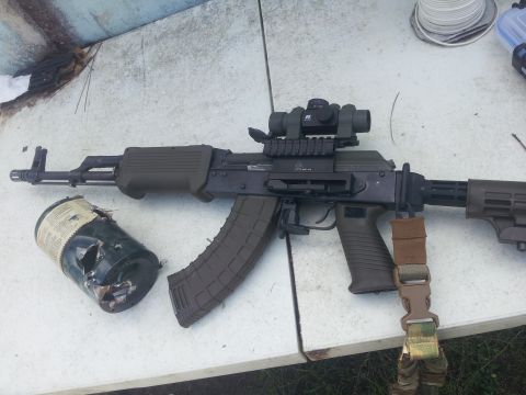 1986 Ford Bronco - An assault rifle with a scope and a damaged canister are placed on a table.