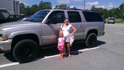 2005 Chevrolet Suburban - A woman and child pose in front of a silver SUV in a parking lot.