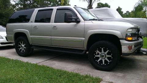 2005 Chevrolet Suburban - Silver SUV parked on a driveway, showing its front quarter and side profile with custom wheels.