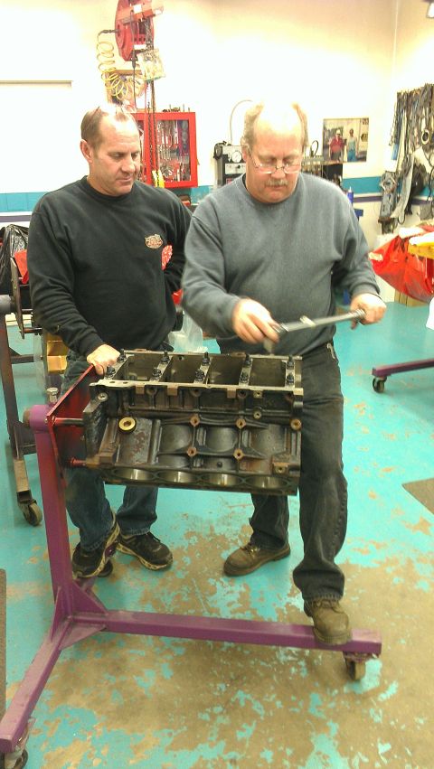 2005 Chevrolet Suburban - Two mechanics examine an engine block mounted on a stand in a workshop.