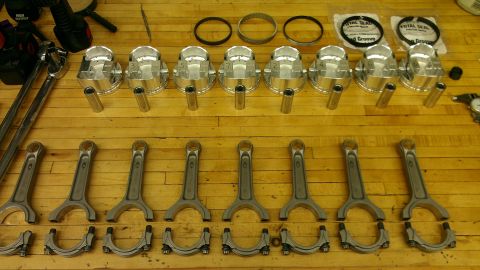 2005 Chevrolet Suburban - Engine parts including pistons, connecting rods, and rings are arranged on a workbench.