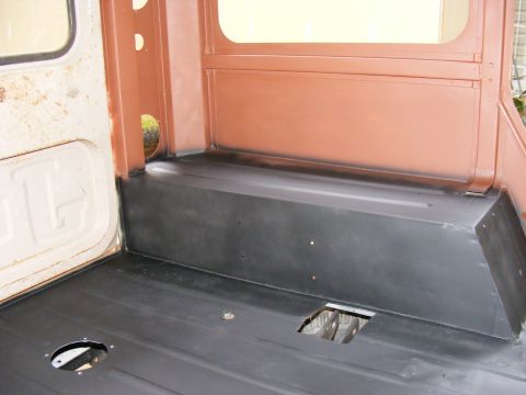 Interior of a vehicle, showing the floor and rear seating area. Black flooring and brown interior panels are v
