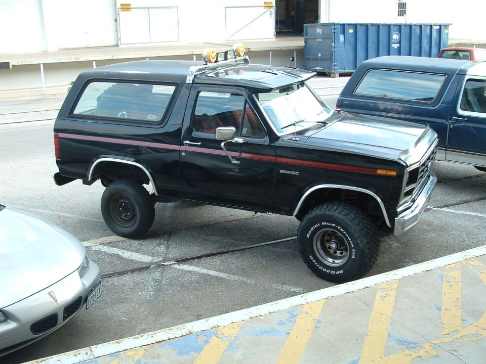 Lifted black Ford Bronco with red stripes, mud-terrain tires, and roof lights parked in a lot
