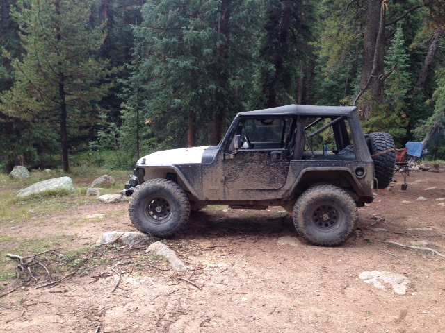 Muddy Jeep Wrangler TJ parked on dirt road in forest