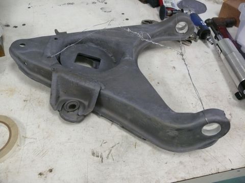 1976 Chevrolet Corvette - A gray suspension control arm is shown with wire wrapped around it, resting on a workbench with tools nearby.