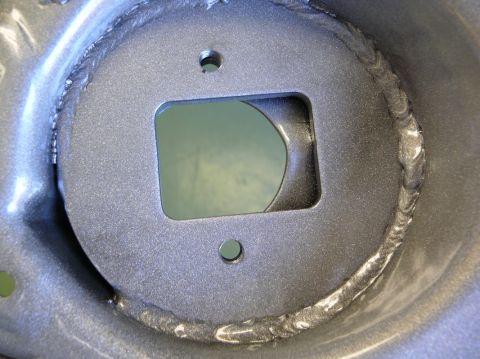 Close-up of a gray metal bracket with a square cutout and two bolt holes, showing rough weld marks around the