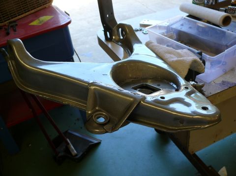 Car suspension control arm hanging from a stand, possibly being cleaned or restored