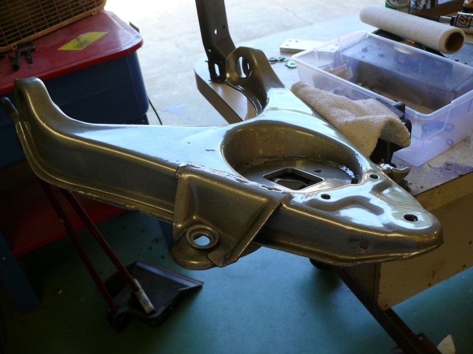Car suspension control arm hanging from a stand, possibly being cleaned or restored