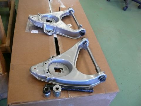 Two aluminum suspension control arms and hardware on a cardboard box