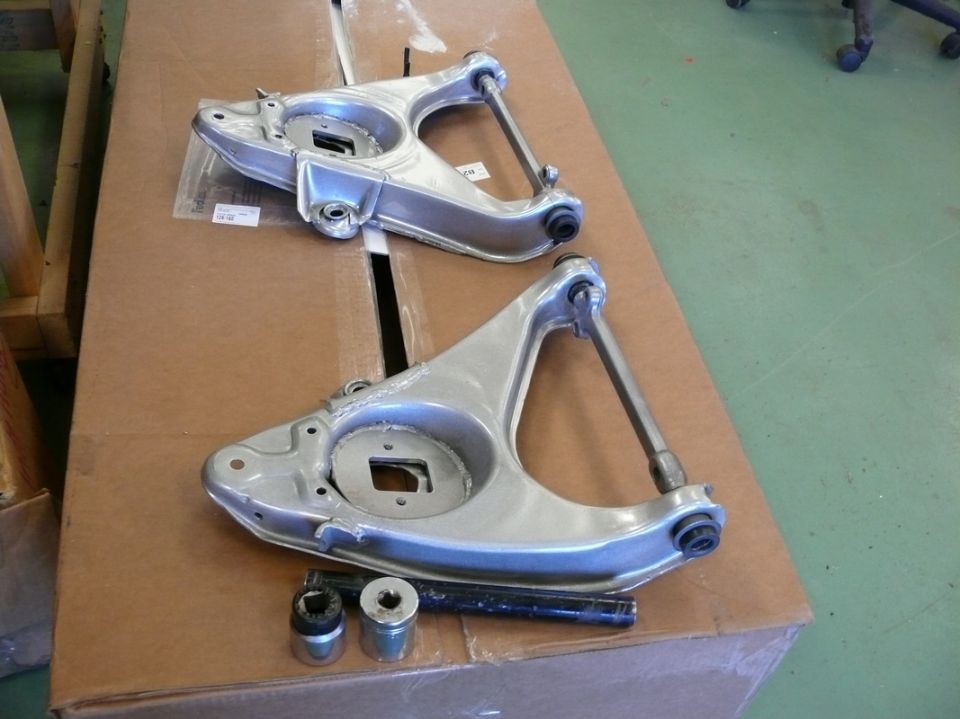 Two aluminum suspension control arms and hardware on a cardboard box