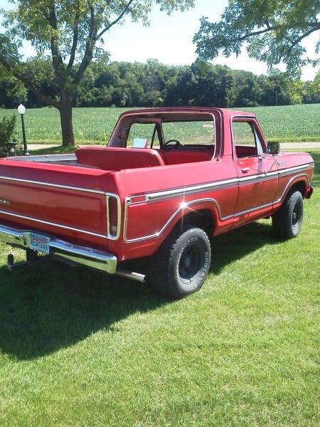 1978 Ford Bronco - A red 1978 Ford Bronco is shown from the rear quarter angle, parked on a grassy lawn with trees and fields in the background.