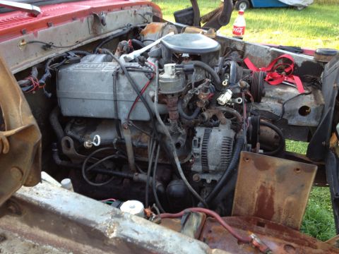 1978 Ford Bronco - The engine bay of a red vehicle shows a V8 engine with visible alternator, hoses, and wiring.