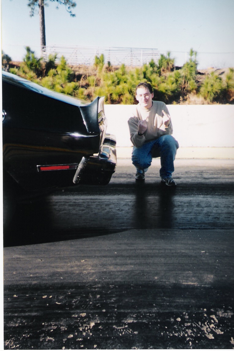 Rear of a black car at a drag strip with a person crouching beside it