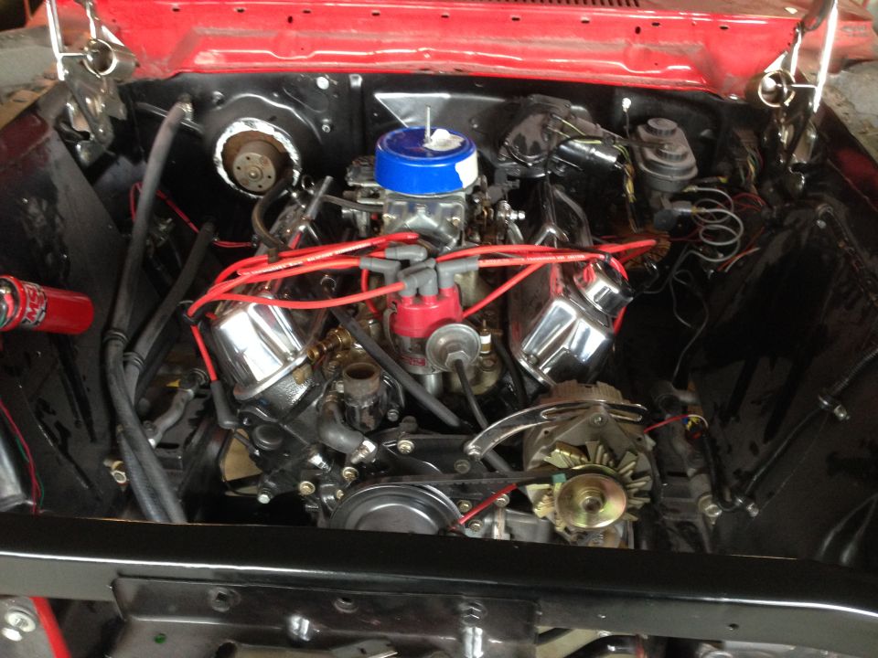 Engine bay of a 1964 Ford Fairlane showing a V8 engine with chrome valve covers and red spark plug wires
