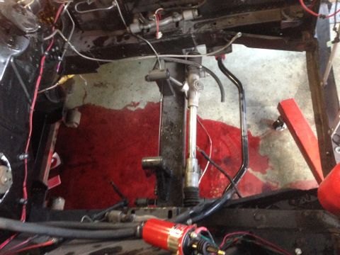 1964 Ford Fairlane - The underbody of a vehicle is shown, the steering column, various wires, and a spill of red fluid on the concrete floor.