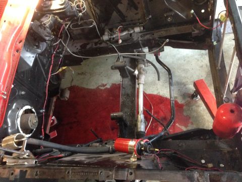 1964 Ford Fairlane - Engine bay undergoing restoration, showing exposed wiring, steering components, and a red fluid spill.