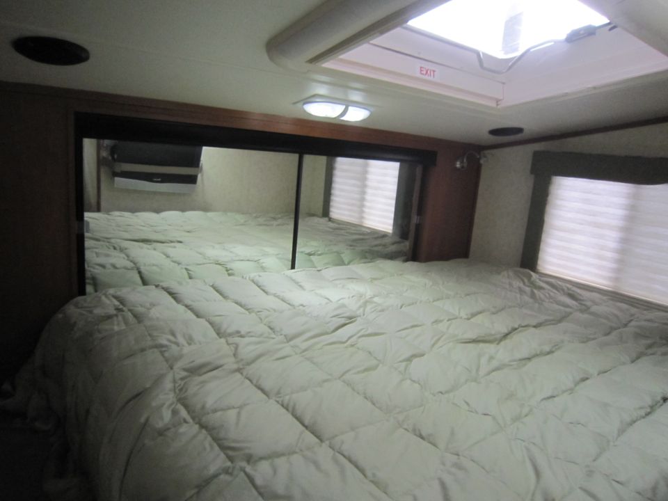 RV bedroom with large bed, mirrored closet doors, and skylight with EXIT sign