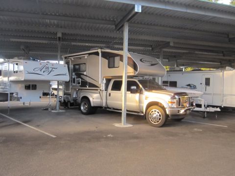 2008 Ford F-450 - A silver 2008 Ford F-450 pickup truck is parked under a covered lot, fitted with a large camper shell.