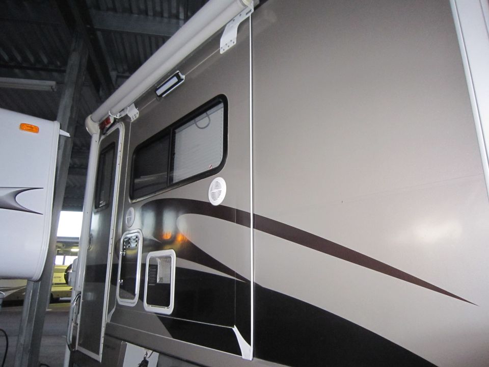 Side view of an RV camper with an awning extended. Another RV is parked next to it
