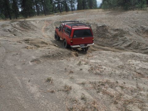 2005 Jeep Wrangler - A red pickup truck navigates a sandy, off-road terrain with trees in the background.