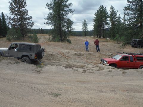 2005 Jeep Wrangler - A gray 2005 Jeep Wrangler is stuck in the sand while a red truck also appears to be stuck nearby.