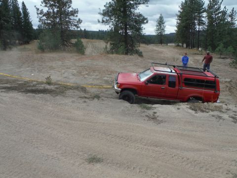 2005 Jeep Wrangler - Red Toyota pickup truck with camper shell is stuck in sand, with two people standing nearby.