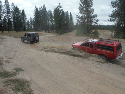 2005 Jeep Wrangler - A Jeep is winching a red pickup truck that is stuck in the mud on an off-road trail.