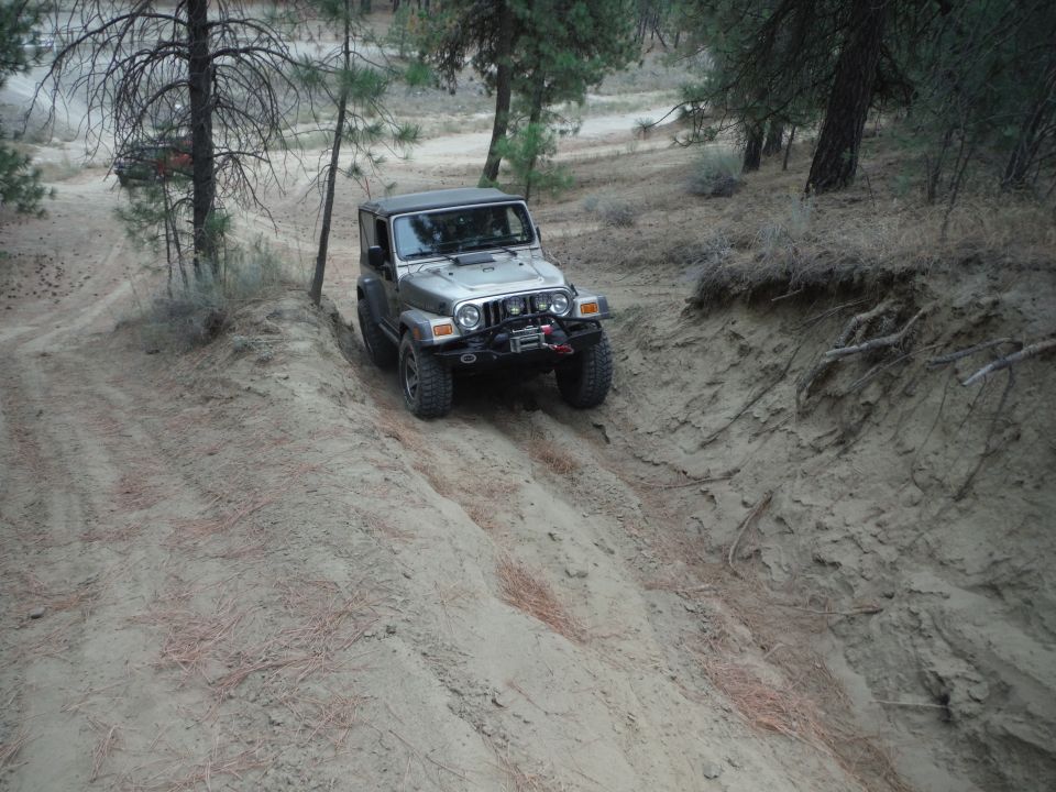 Silver 2005 Jeep Wrangler driving on a sandy hill with a winch