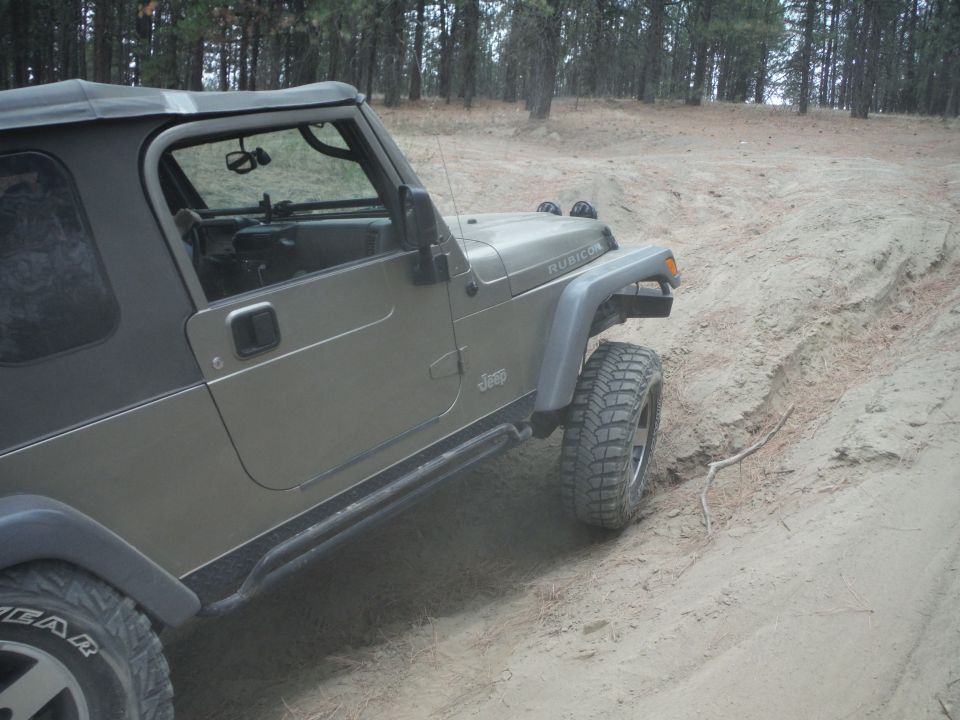 Tan Jeep Wrangler Rubicon on a dirt trail, right front tire angled up a sandy embankment