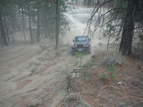 2005 Jeep Wrangler - A Jeep Wrangler navigates a dusty, off-road trail surrounded by trees and dry brush.
